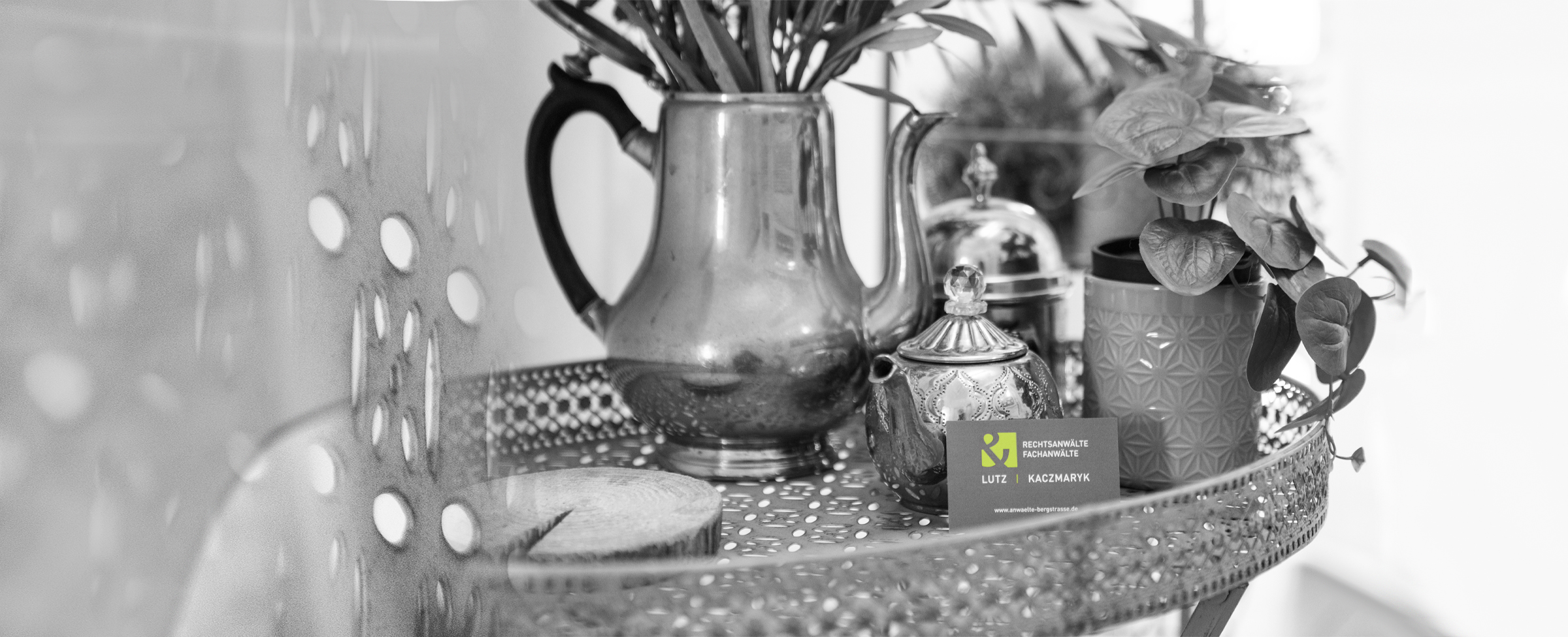 Ein Stillfoto mit einem Ensemble aus antiken Kännchen und Blumen stehend auf einem verzierten Tabletttisch. Im Vordergrund stehen Kanzleivisitenkarten