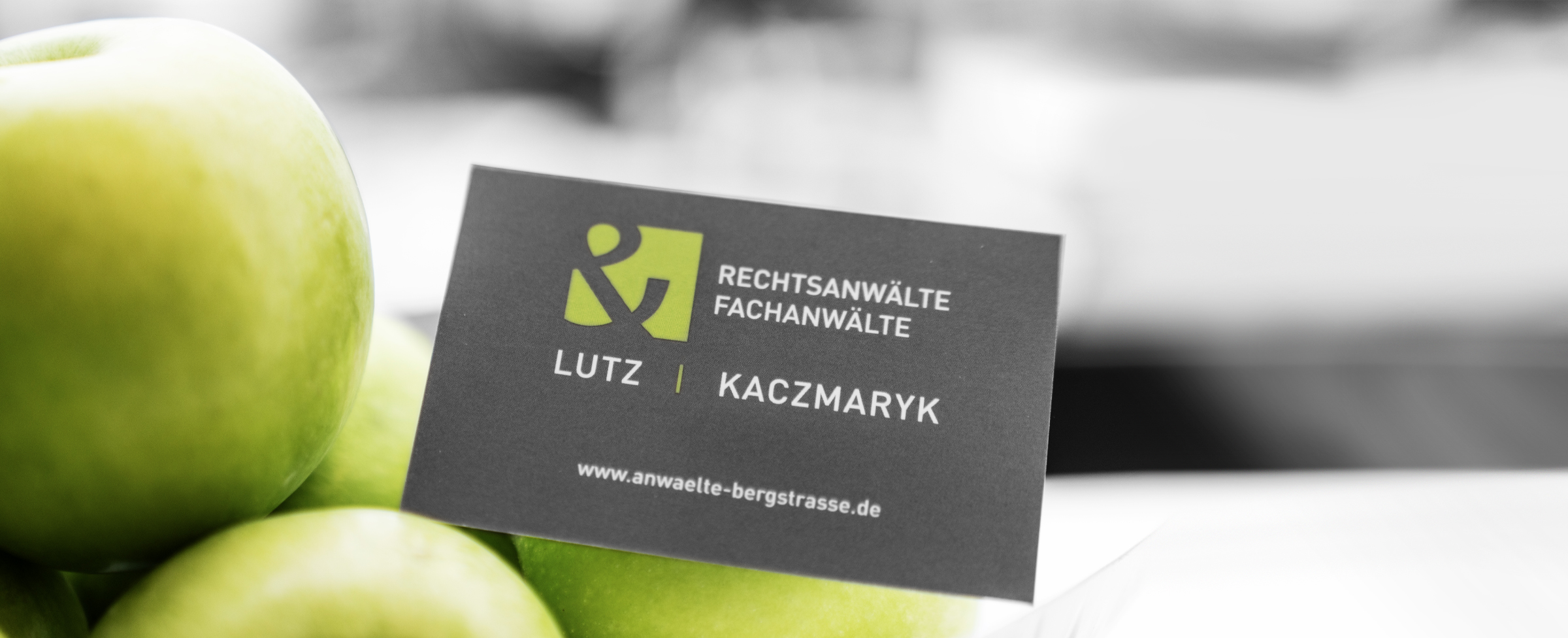 Eine Kanzleivisitenkarte steht auf einer Ansammlung grüner Äpfel. Stimmungsvolle Aufnahme