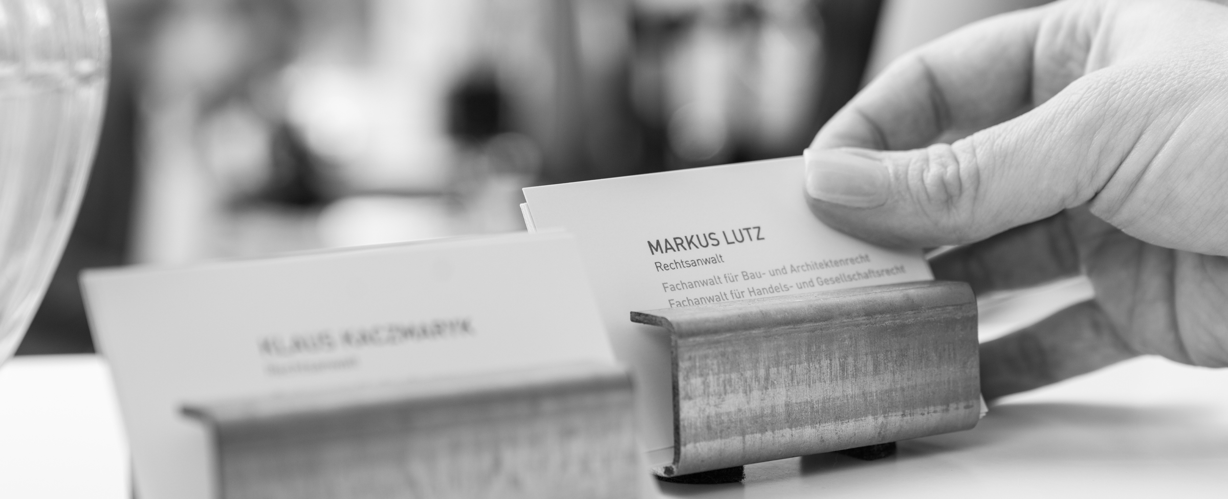 Eine weibliche Hand nimmt sich eine Visitenkarte aus einem der beiden Visitenkartenhalter. Der Hintergrund ist stimmungsvoll verschwommen