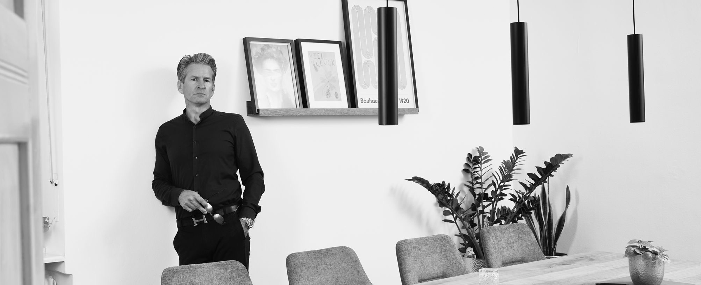 Rechtsanwalt Markus Lutz lehnt an einer Wand. Er blickt in die Kamera. Im Raum steht ein großer Tisch mit Stühlen. Bilder hängen an der Wand. Einladendes Ambiente